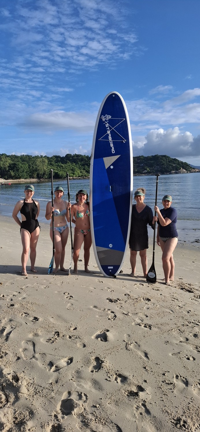 Retreat guests with a paddleboard on the beach in Koh Samui