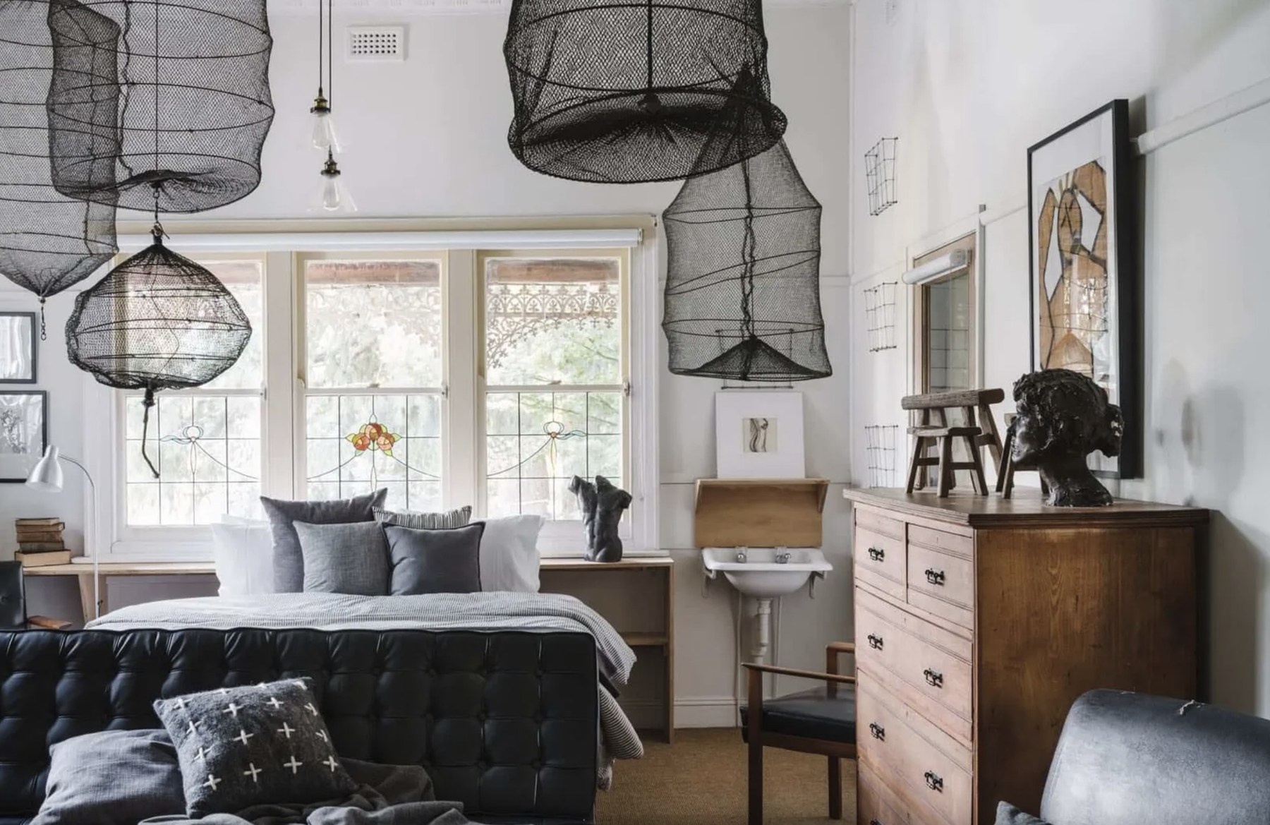 A character-filled bedroom at The Oxford in Hepburn Springs, with stained-glass windows and sculptural pendant lights
